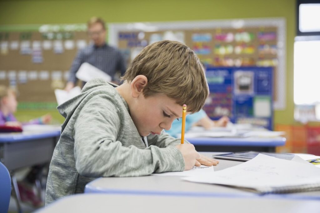 Un garçon assis à son bureau dans une salle de classe qui travaille efficacement et réussit grâce à l'aide reçue