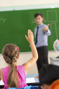 Une jeune fille à l'école qui lève la main en classe, confiante. La psychothérapie: des bienfaits à tous les âges!